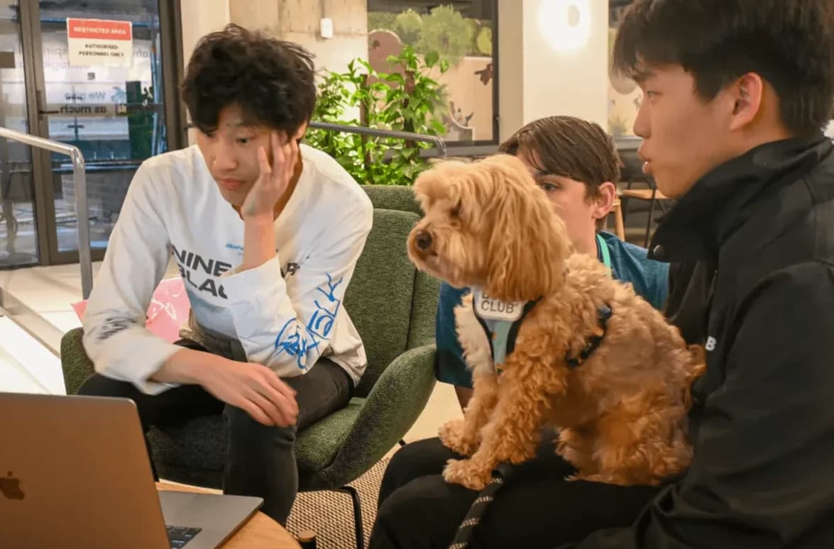 Three members build together on a couch while a dog watches the screen.